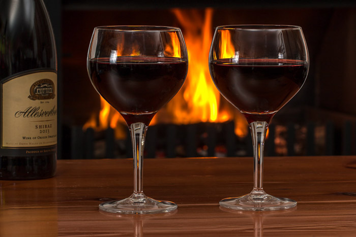 A photo of a bottle of wine and two glasses with a fire in the background